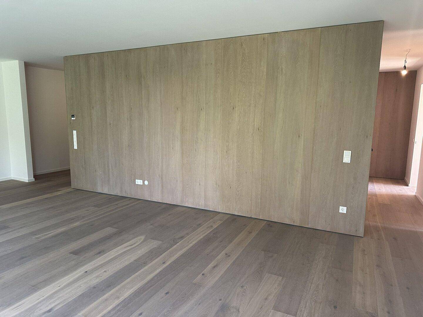 Heller, leerer Raum mit elegantem Holzparkett und einer markanten Holzwand als Raumteiler.