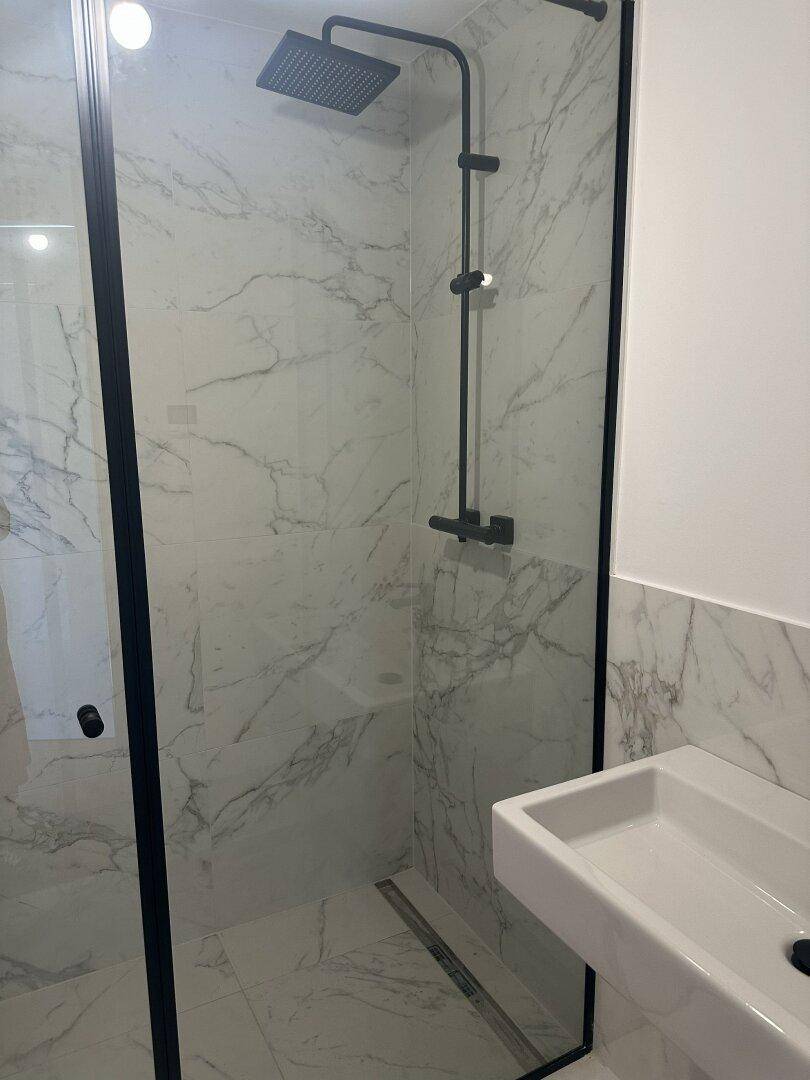 Modernes Badezimmer mit begehbarer Dusche, Marmorfliesen und schwarzen Armaturen.