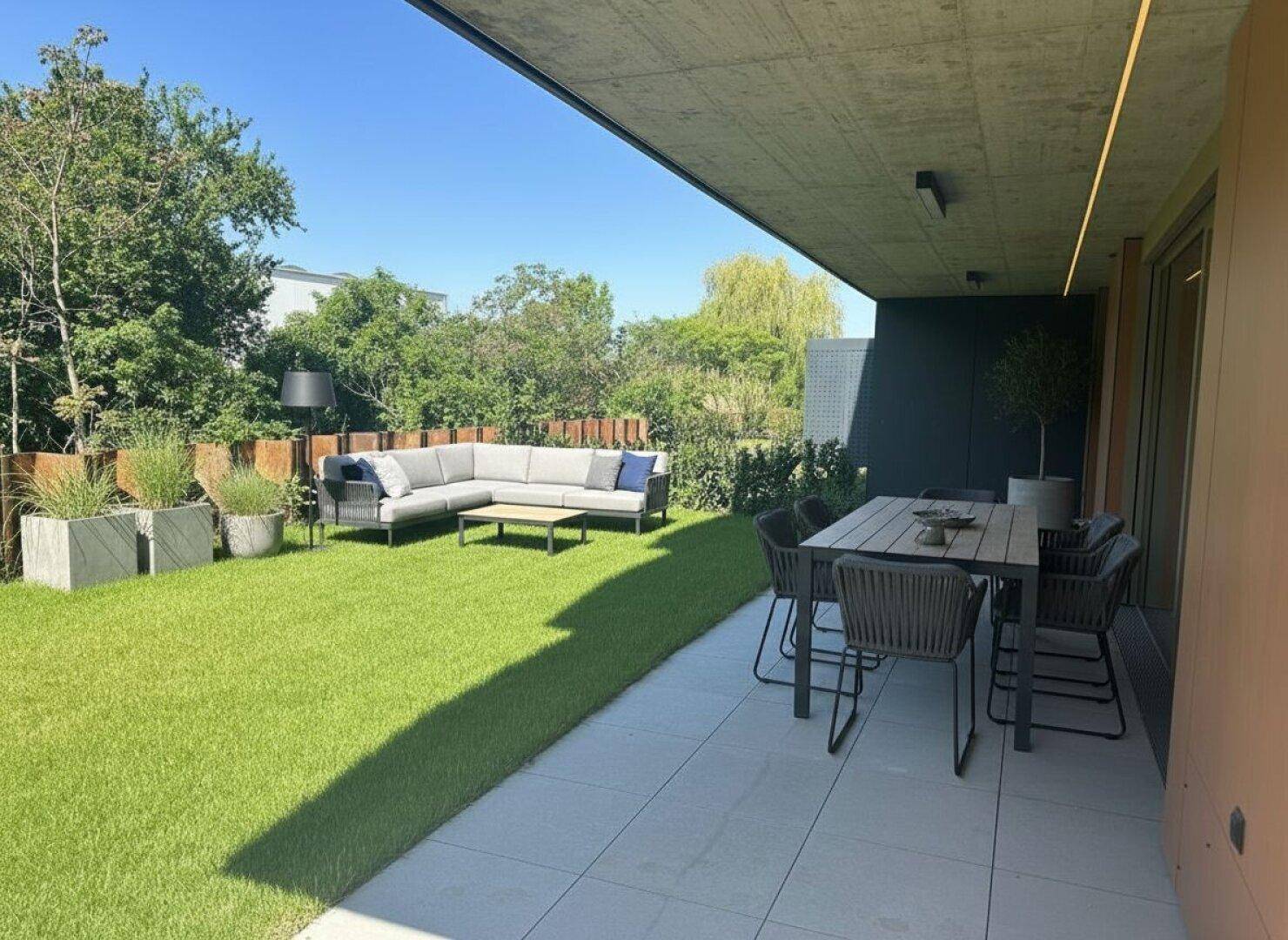 Großzügiger Gartenbereich mit Rasenfläche, moderner Lounge und Essbereich unter einer überdachten Terrasse.