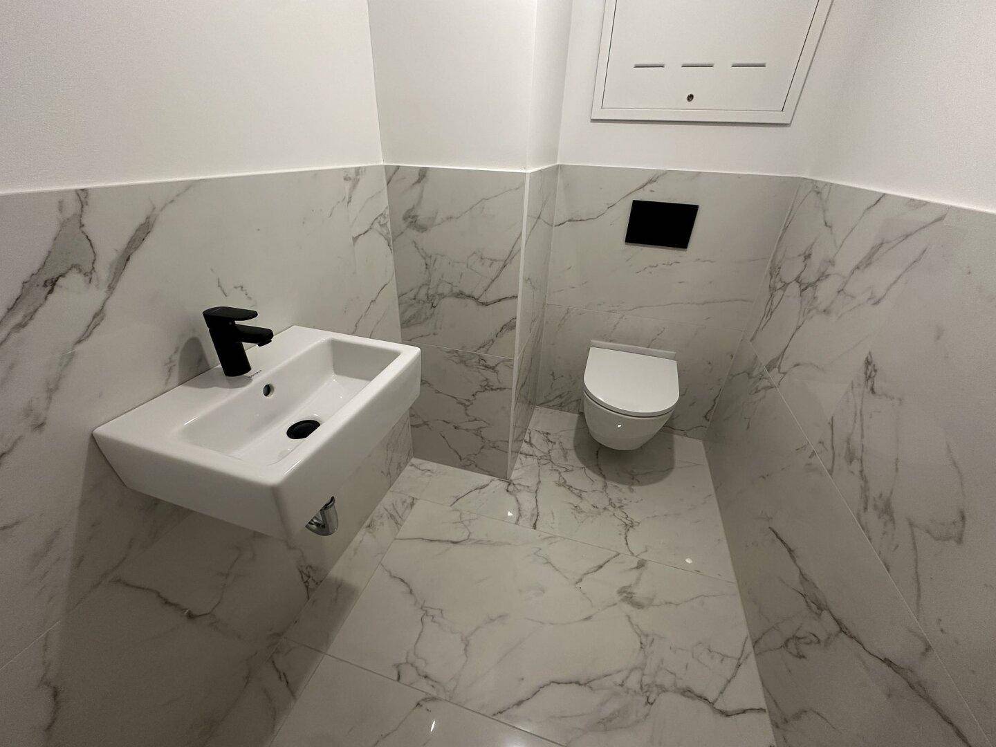 Stilvolles Gäste-WC mit Wand-WC, modernem Waschbecken und Marmoroptik-Fliesen.