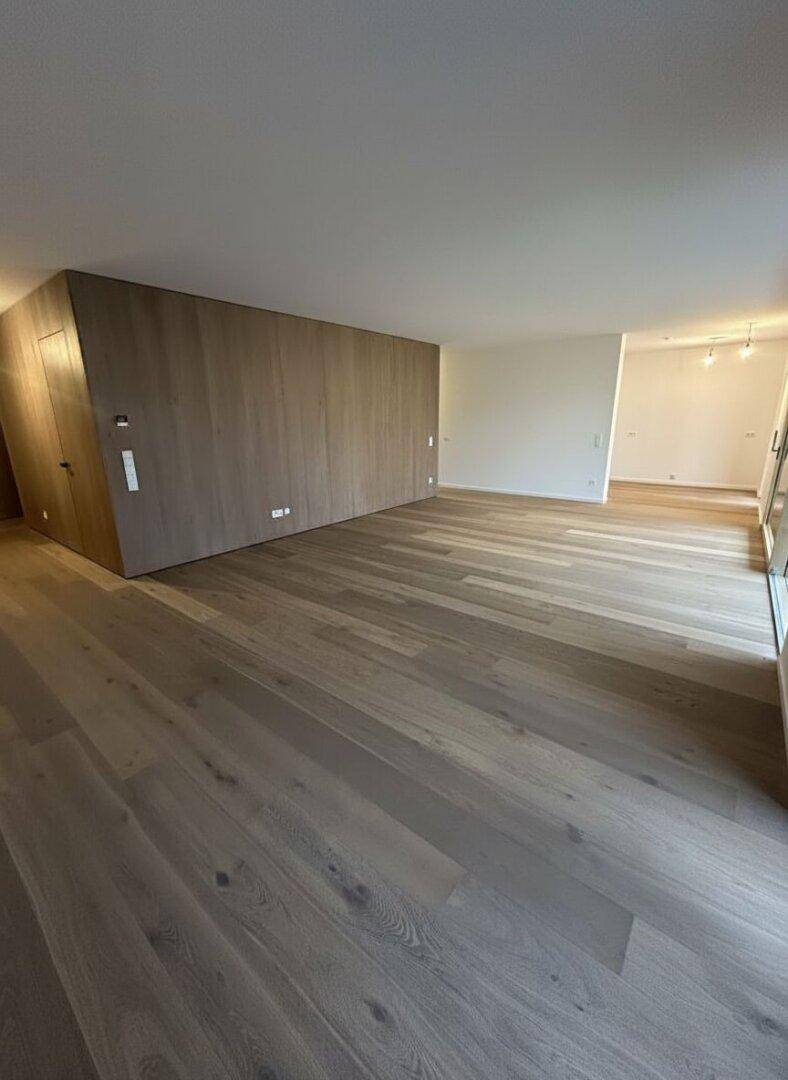 Geräumiger, unmöblierter Wohnbereich mit hellem Holzparkett und moderner Holzwandverkleidung.