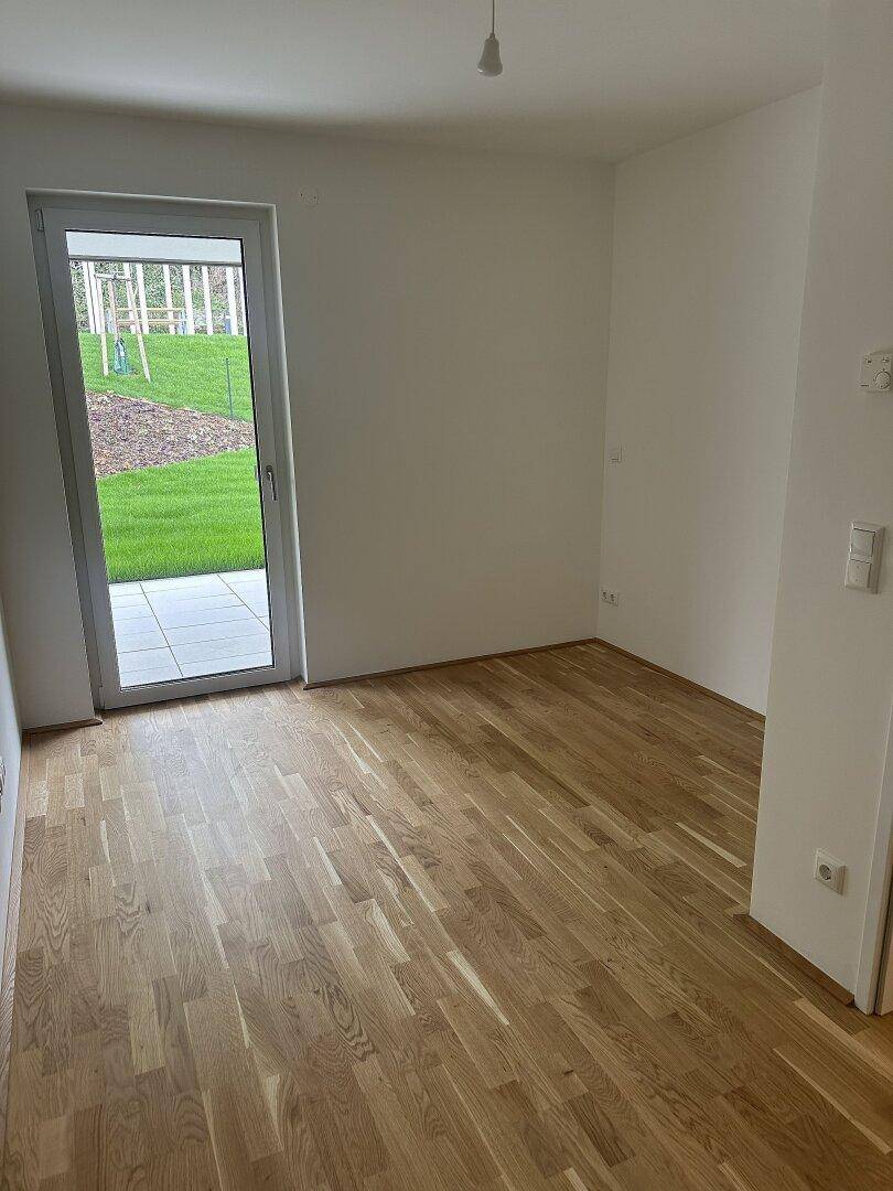 Heller Raum mit Eichenparkett und Zugang zu einer Terrasse oder einem Gartenbereich.