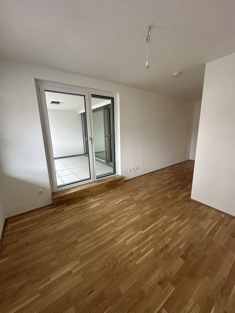 Geräumiger Raum mit Holzboden und Schiebetür zu einem Balkon oder einer Loggia.