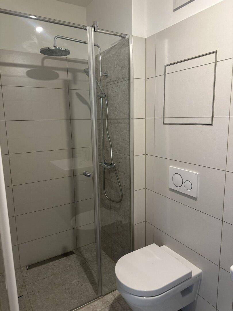 Modernes Badezimmer mit ebenerdiger Dusche und Wand-WC, in hellen Fliesen gehalten.