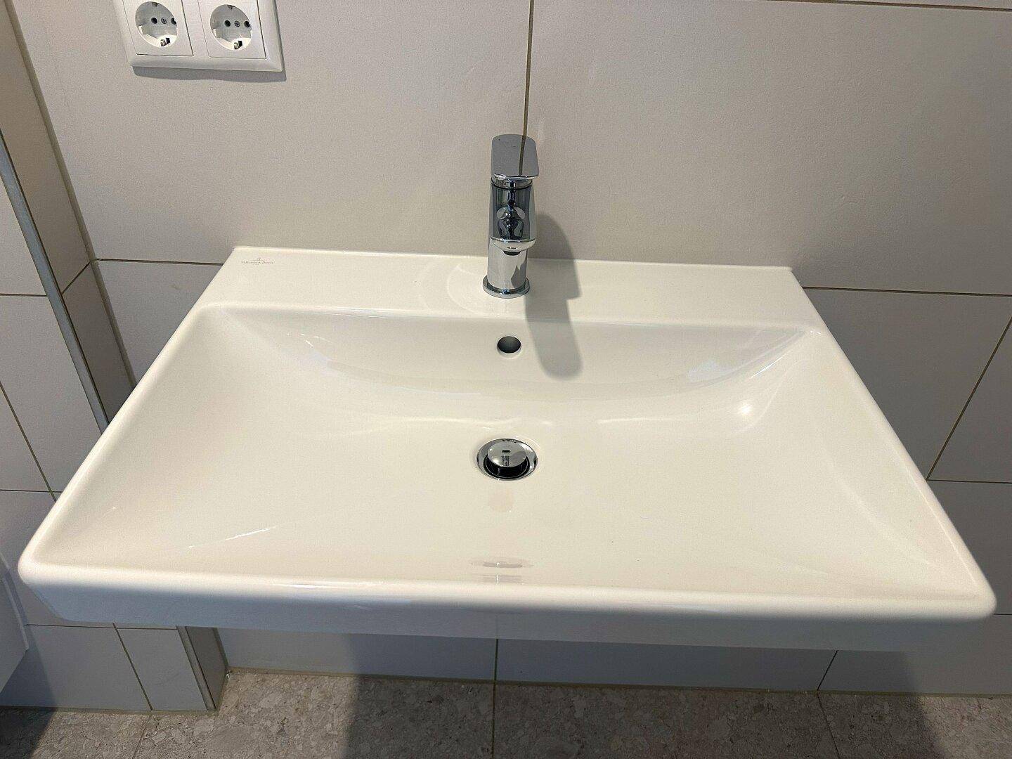 Modernes Waschbecken mit elegantem Wasserhahn in einem hell gefliesten Badezimmer.