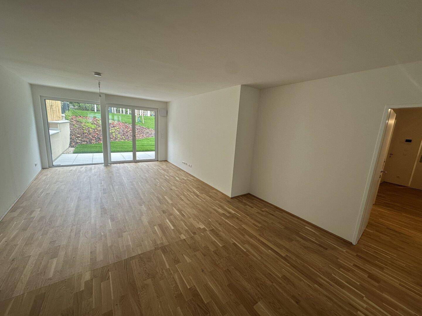 Geräumiger Wohnbereich mit Holzboden und großen Fenstern zum Garten, ideal für helle Einrichtung.