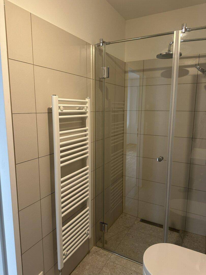 Modernes Badezimmer mit ebenerdiger Dusche und beheiztem Handtuchhalter, hell gefliest.