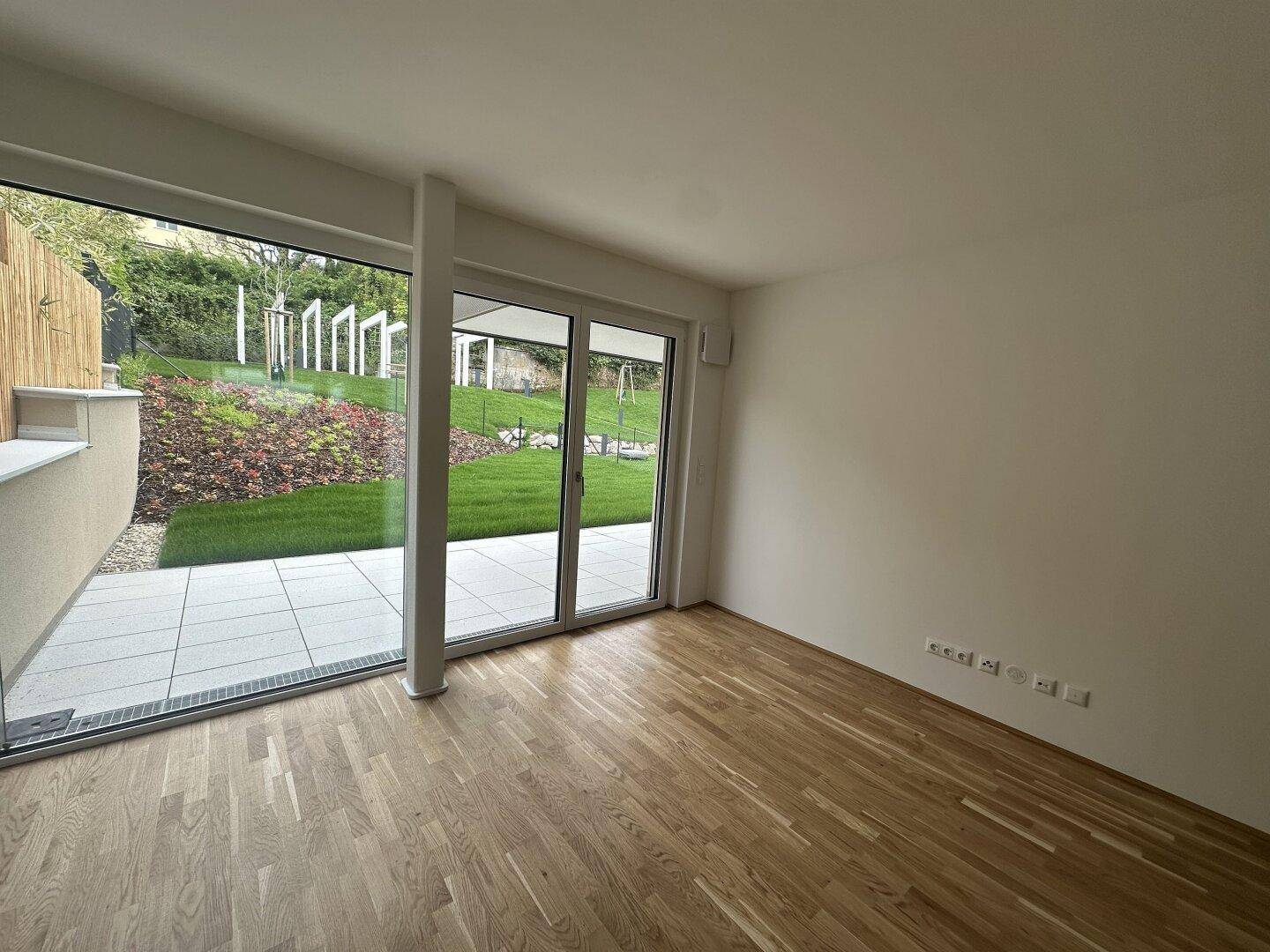 Heller Raum mit Holzboden und großen Schiebetüren, die zum Gartenbereich führen.