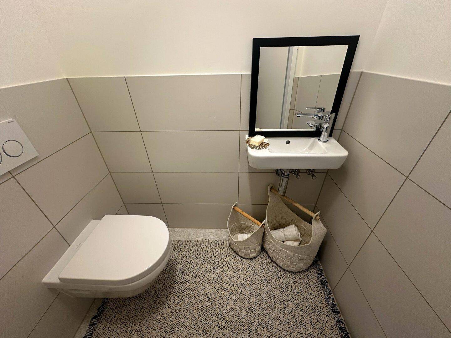 Kleines Gäste-WC mit Wand-WC, kleinem Waschbecken und Fliesenboden.