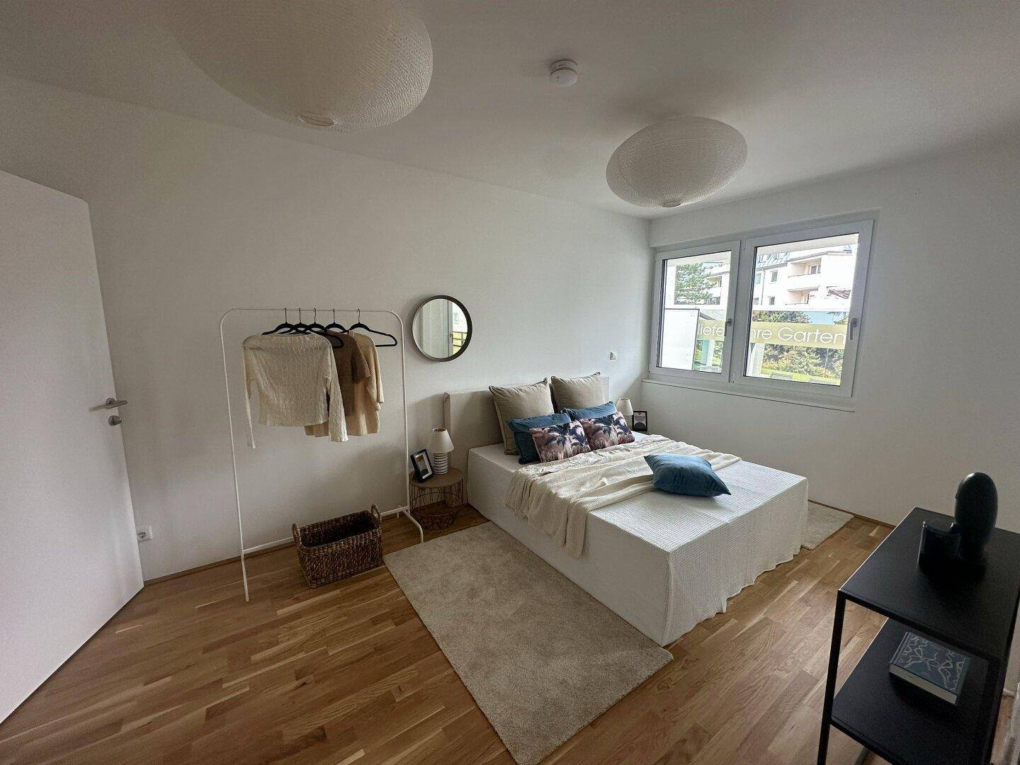 Helles Schlafzimmer mit Holzboden, minimalistischer Einrichtung und großem Fenster.