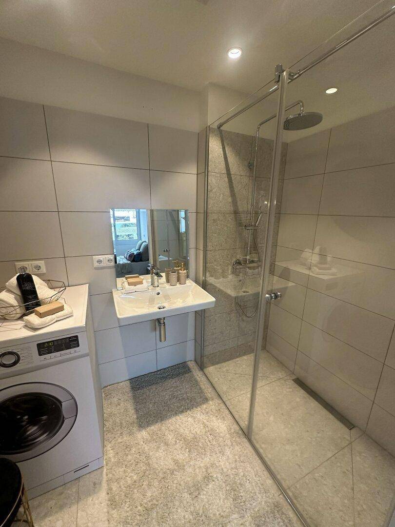 Modernes Badezimmer mit begehbarer Dusche, Waschbecken und Waschmaschine.