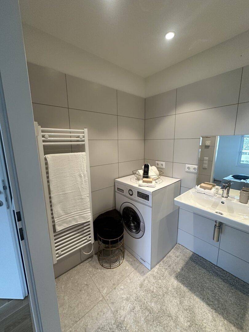 Funktionales Badezimmer mit Waschmaschine, beheiztem Handtuchhalter und modernem Waschbecken.