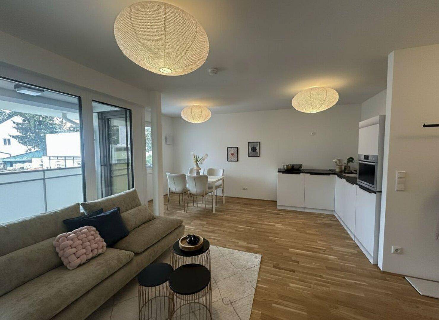 Lichtdurchfluteter Wohn-Essbereich mit Holzboden, moderner Einrichtung und Zugang zum Balkon.