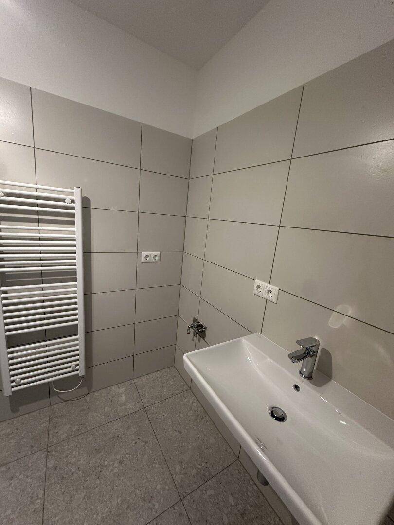 Modernes Badezimmer mit grauen Fliesen, Einzelwaschbecken und beheiztem Handtuchhalter.