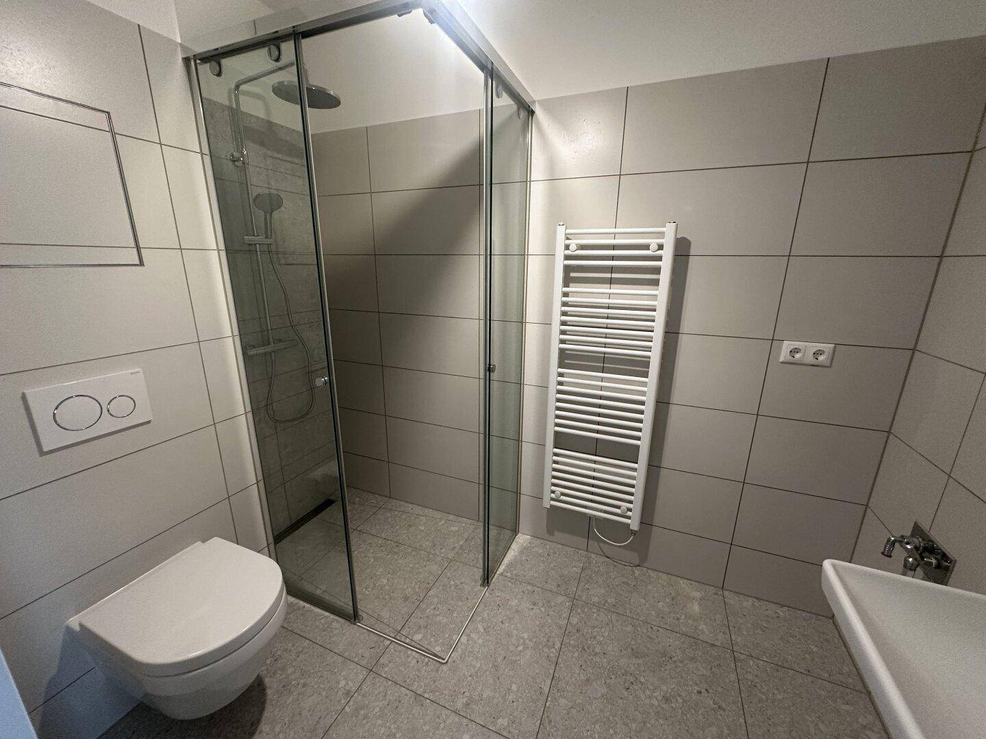 Funktionales Badezimmer mit begehbarer Dusche, WC, Einzelwaschbecken und beheiztem Handtuchhalter.