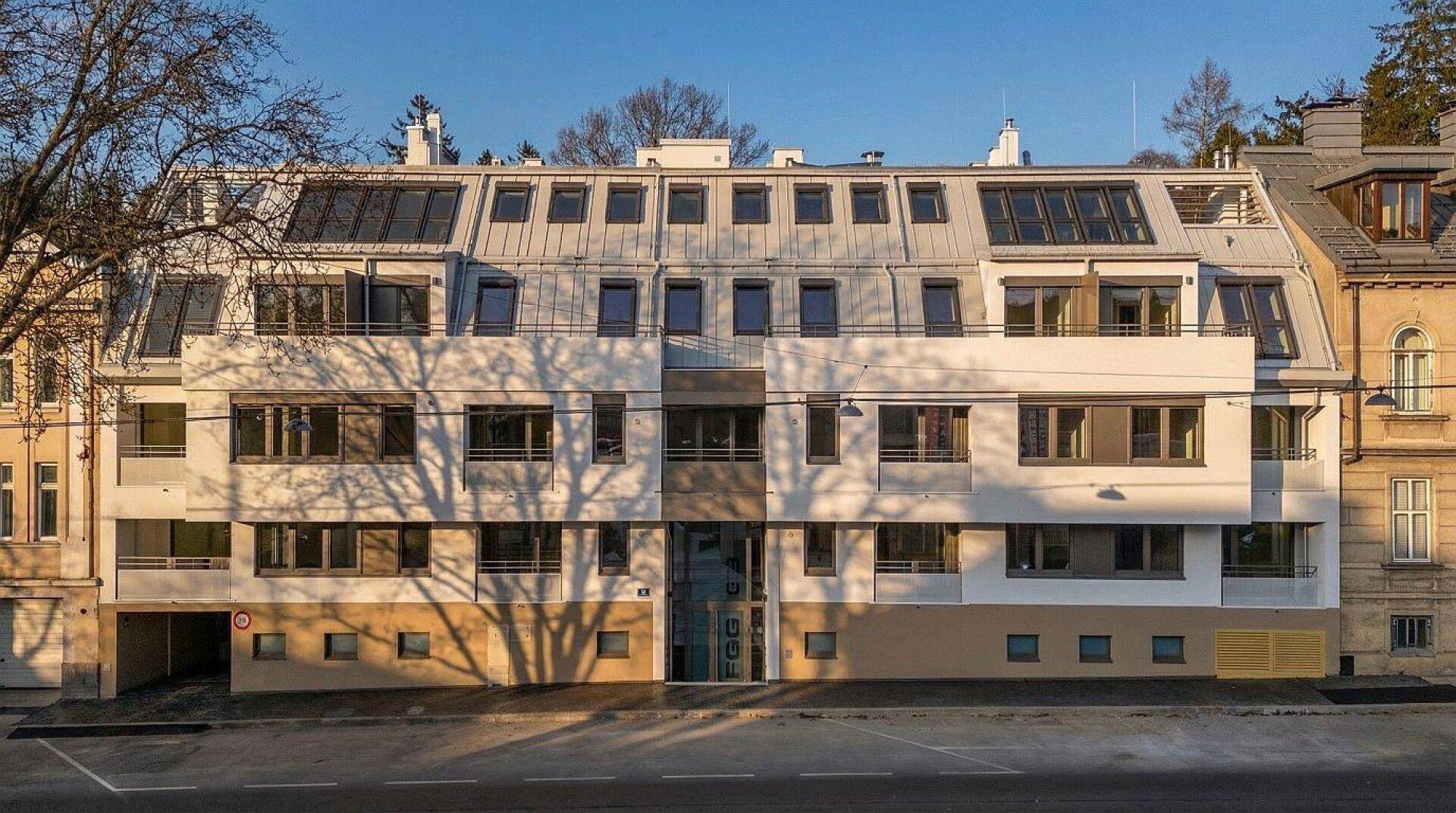 Moderne Fassade eines Mehrfamilienhauses mit zahlreichen Fenstern und Balkonen unter blauem Himmel.