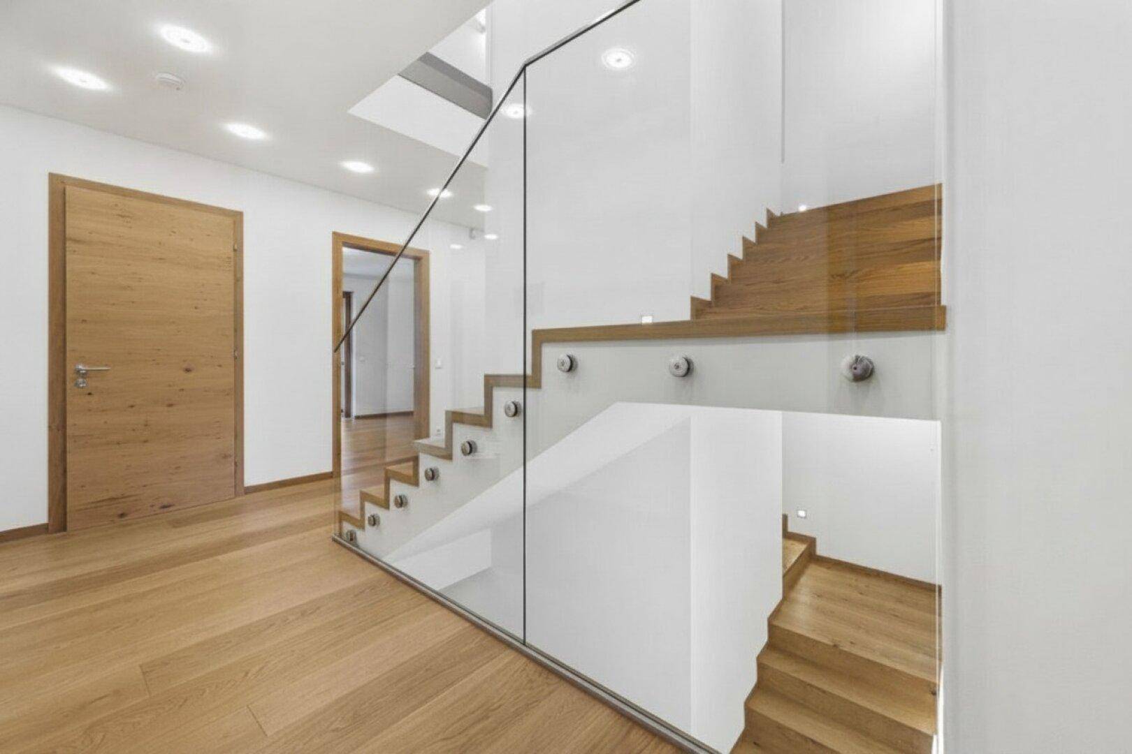 Heller Flur mit moderner Holztreppe und elegantem Glasgeländer, führt zu den oberen Etagen des Hauses.