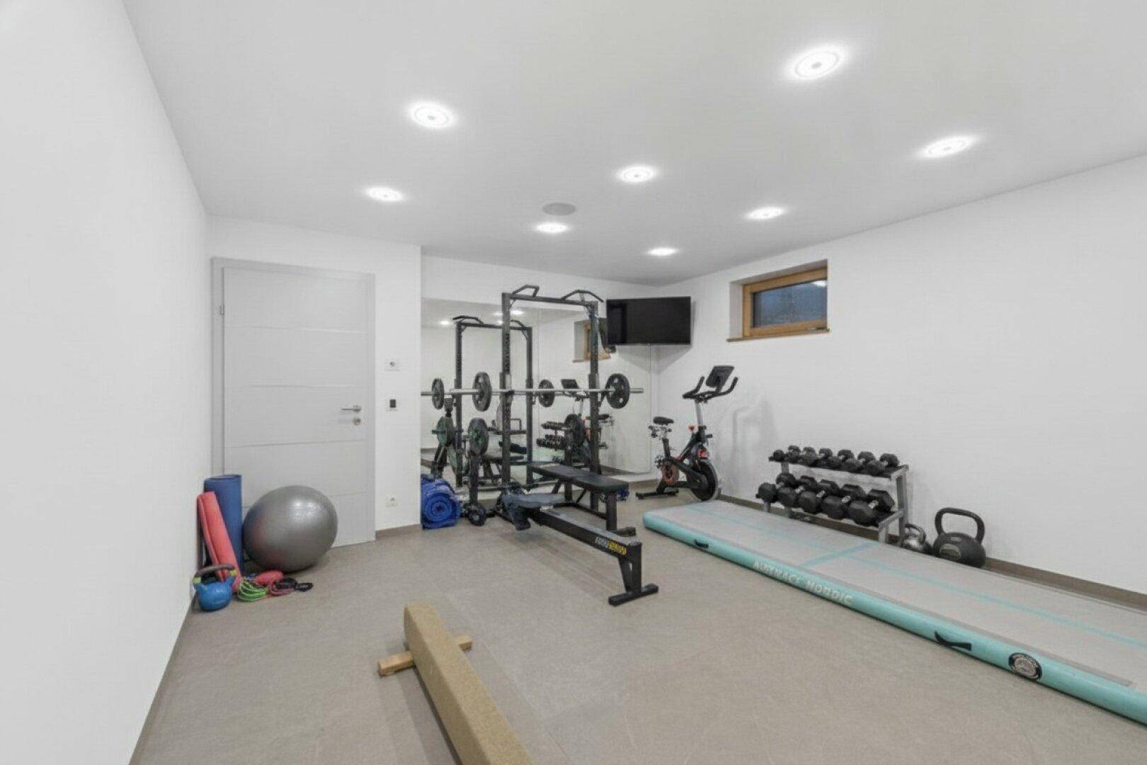 Gut ausgestatteter Fitnessraum im Untergeschoss mit verschiedenen Trainingsgeräten und Fenster.