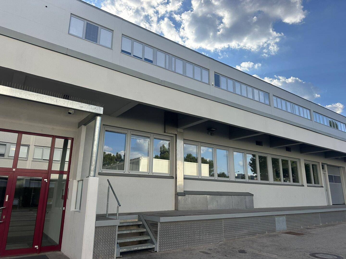 Moderne Gebäudefassade mit großen Fenstern und einem Eingangsbereich mit roter Tür.