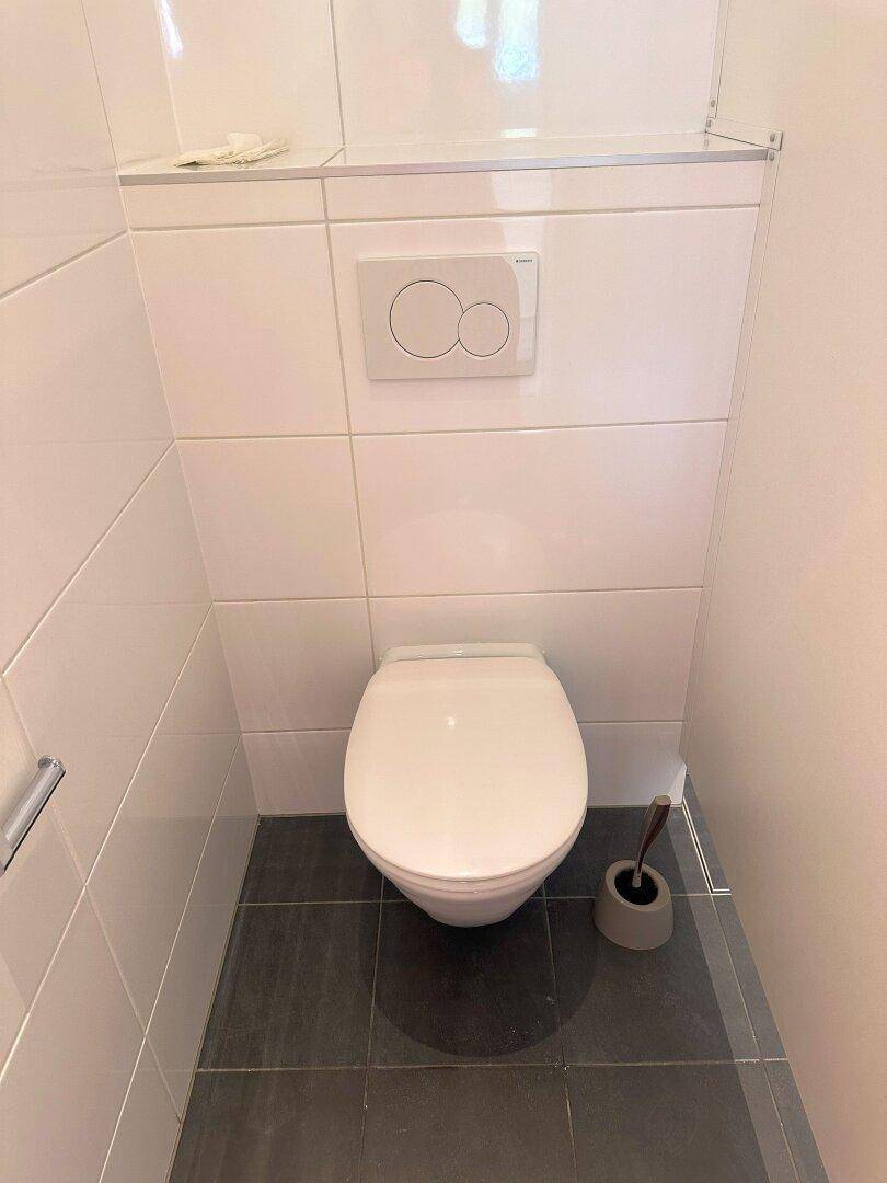Modernes Gäste-WC mit wandhängendem WC, weiß gefliesten Wänden und dunklem Boden.