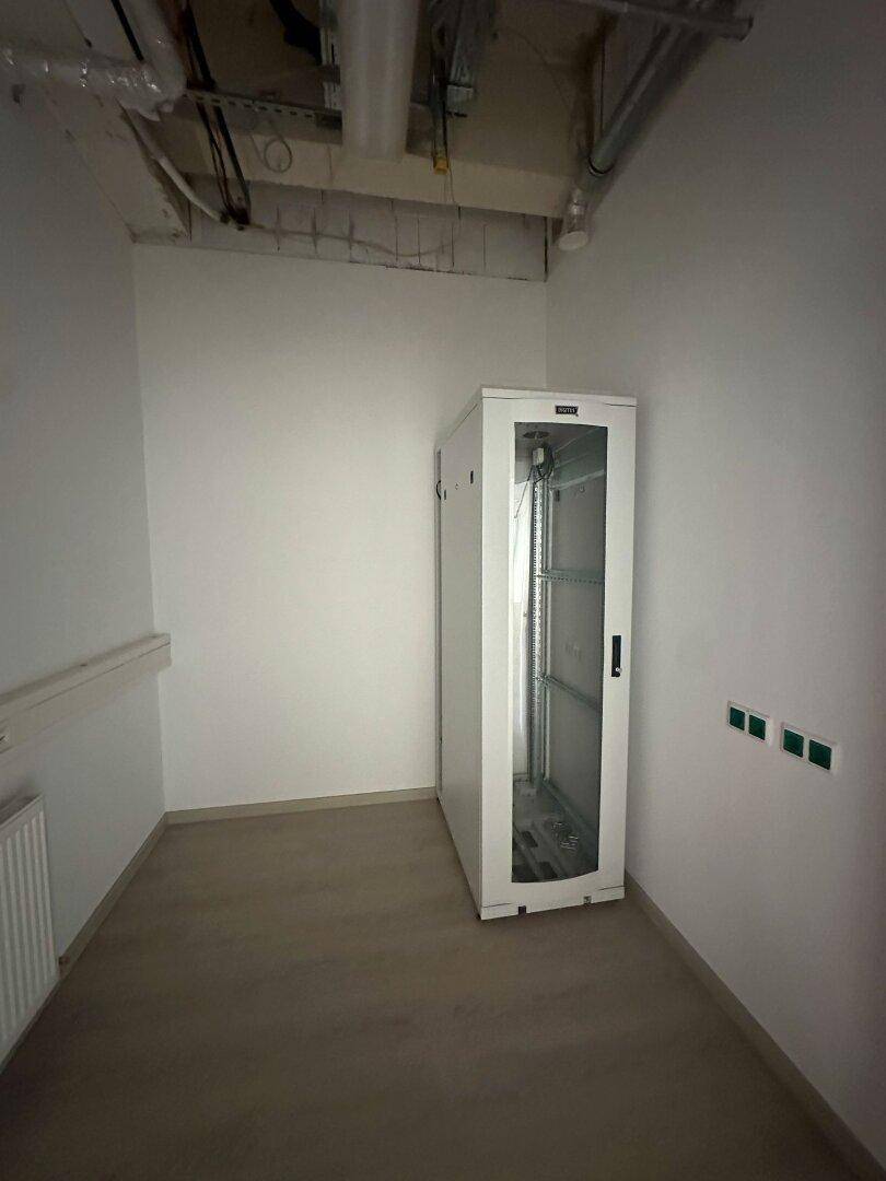 Kleiner Serverraum mit einem Serverschrank, Laminatboden und sichtbaren Deckeninstallationen.