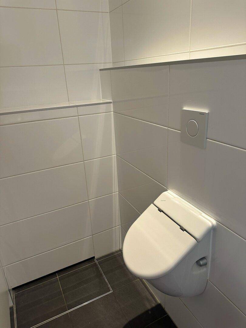 Modernes Gäste-WC mit wandhängendem WC, weiß gefliesten Wänden und dunklem Boden.