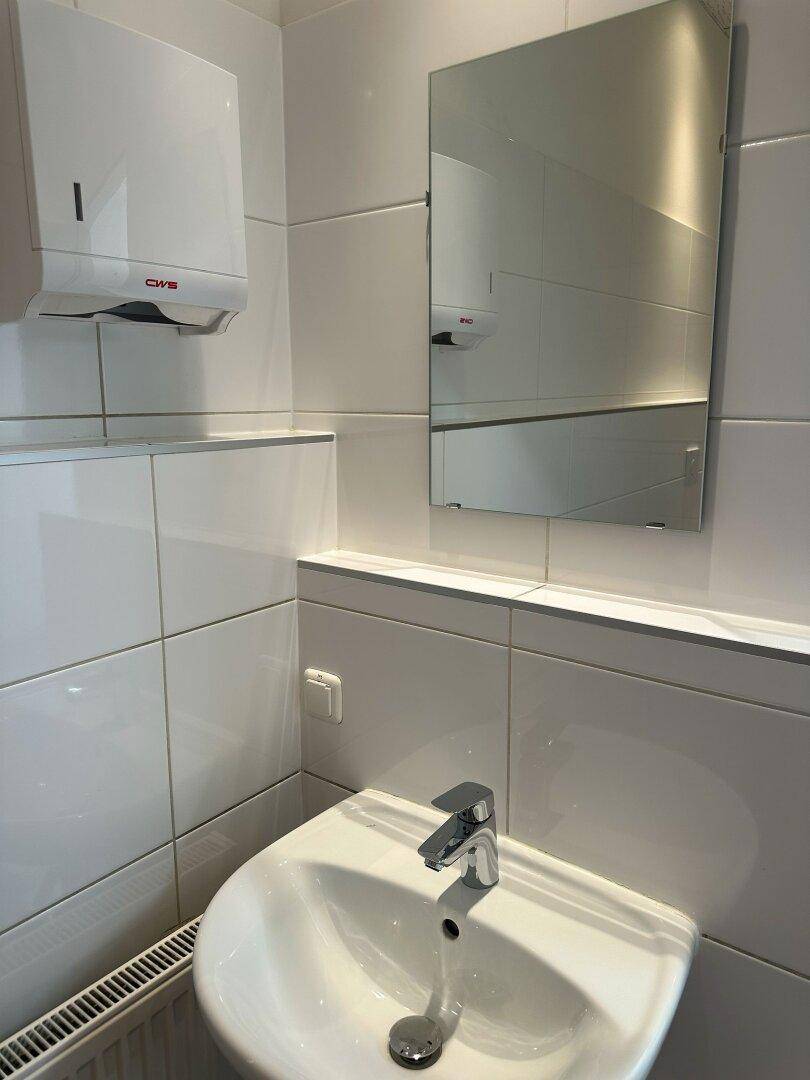 Modernes Gäste-WC mit weiß gefliesten Wänden, Waschbecken und Spiegel.