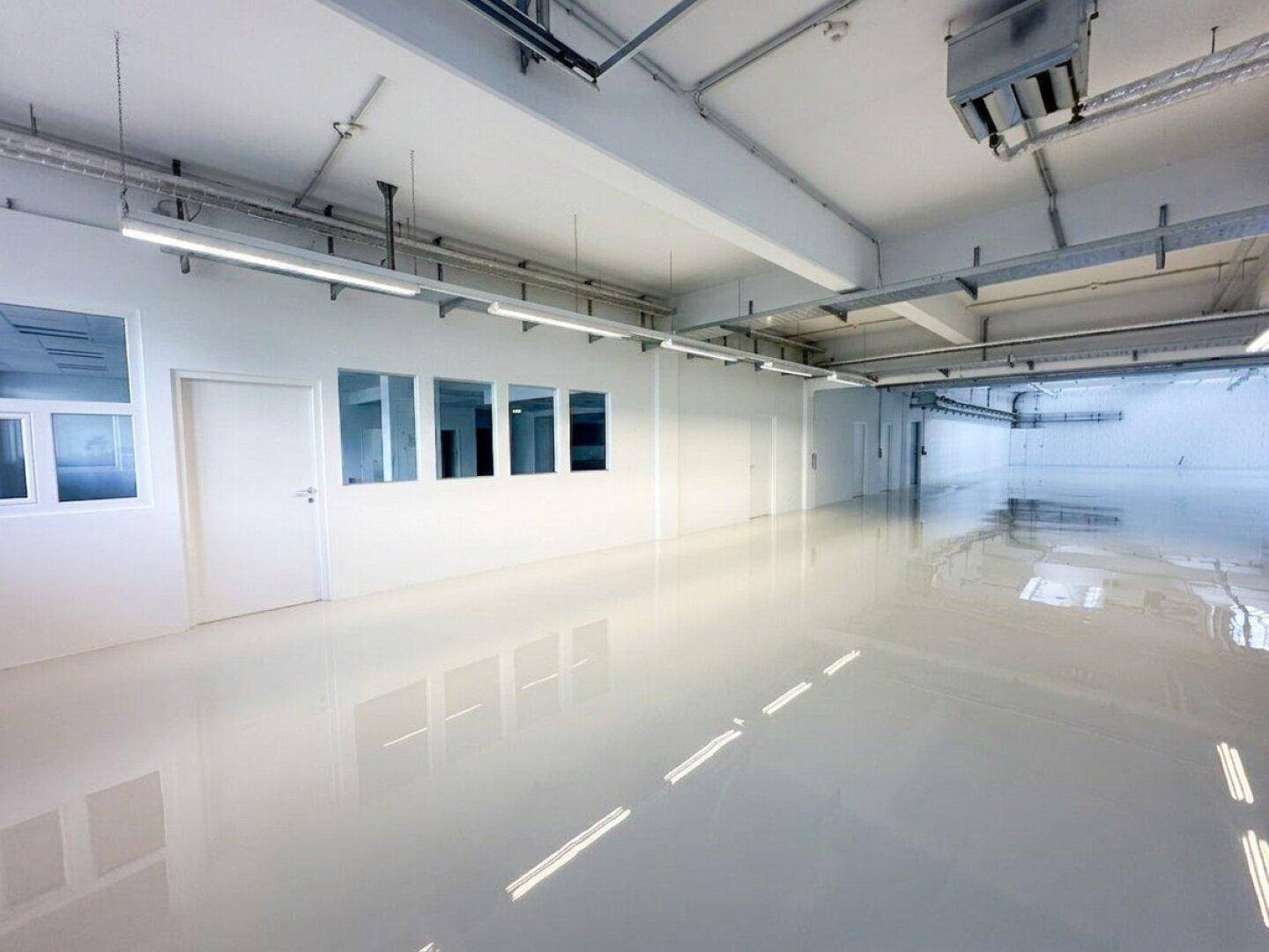 Großer, heller Industrieraum mit glänzendem Boden, sichtbaren Leitungen und hohen Decken.