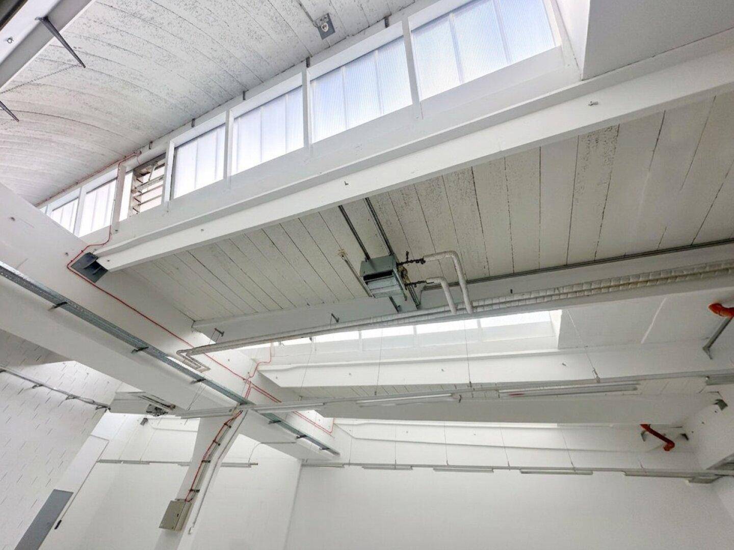 Industrielle Deckenkonstruktion mit sichtbaren Trägern, Leitungen und Oberlichtern.