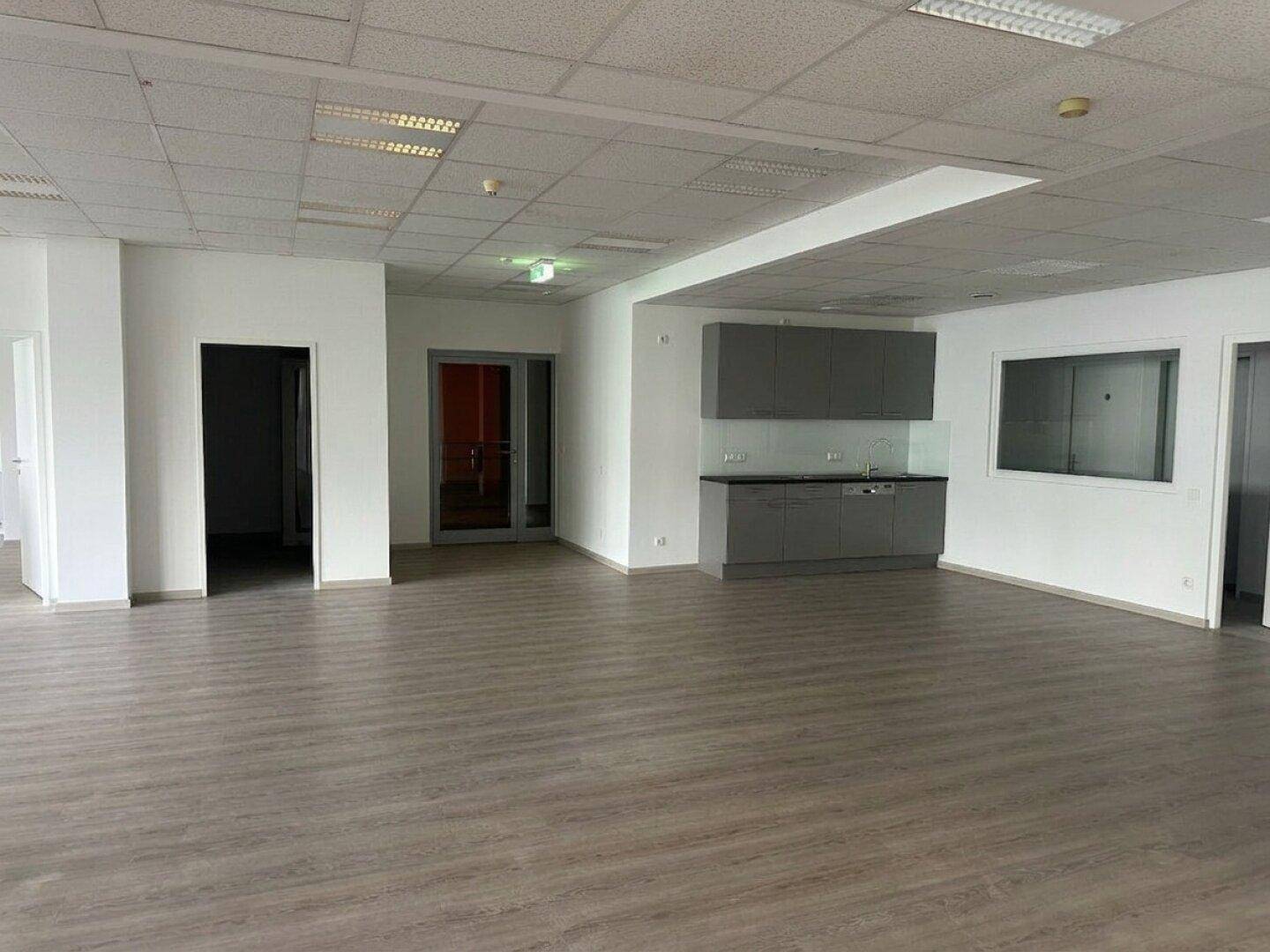 Offener Bürobereich mit Laminatboden und einer kleinen Küchenzeile mit grauen Schränken.