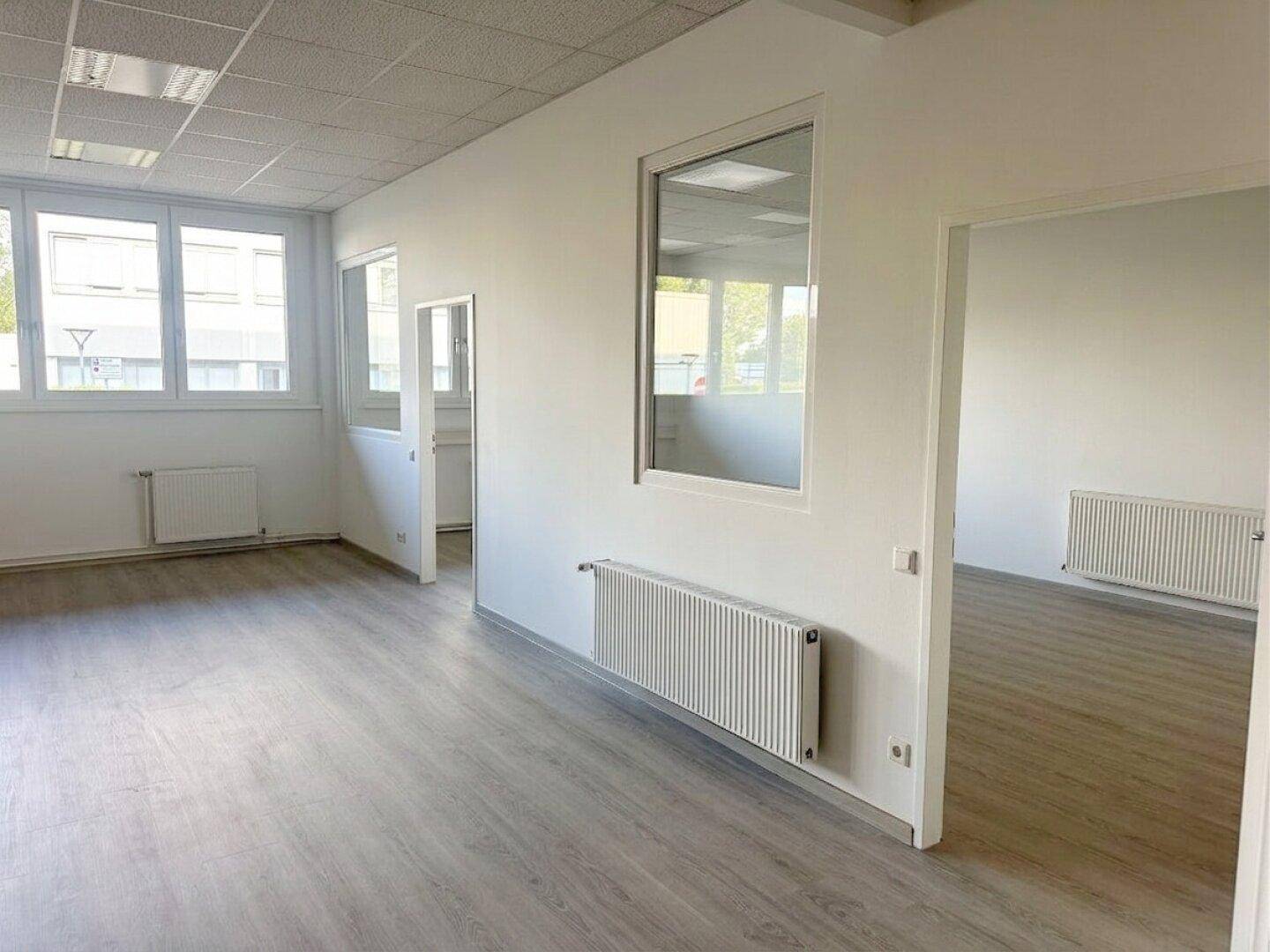 Helles Büro mit Laminatboden, Heizkörpern und großen Fenstern, die viel Licht hereinlassen.