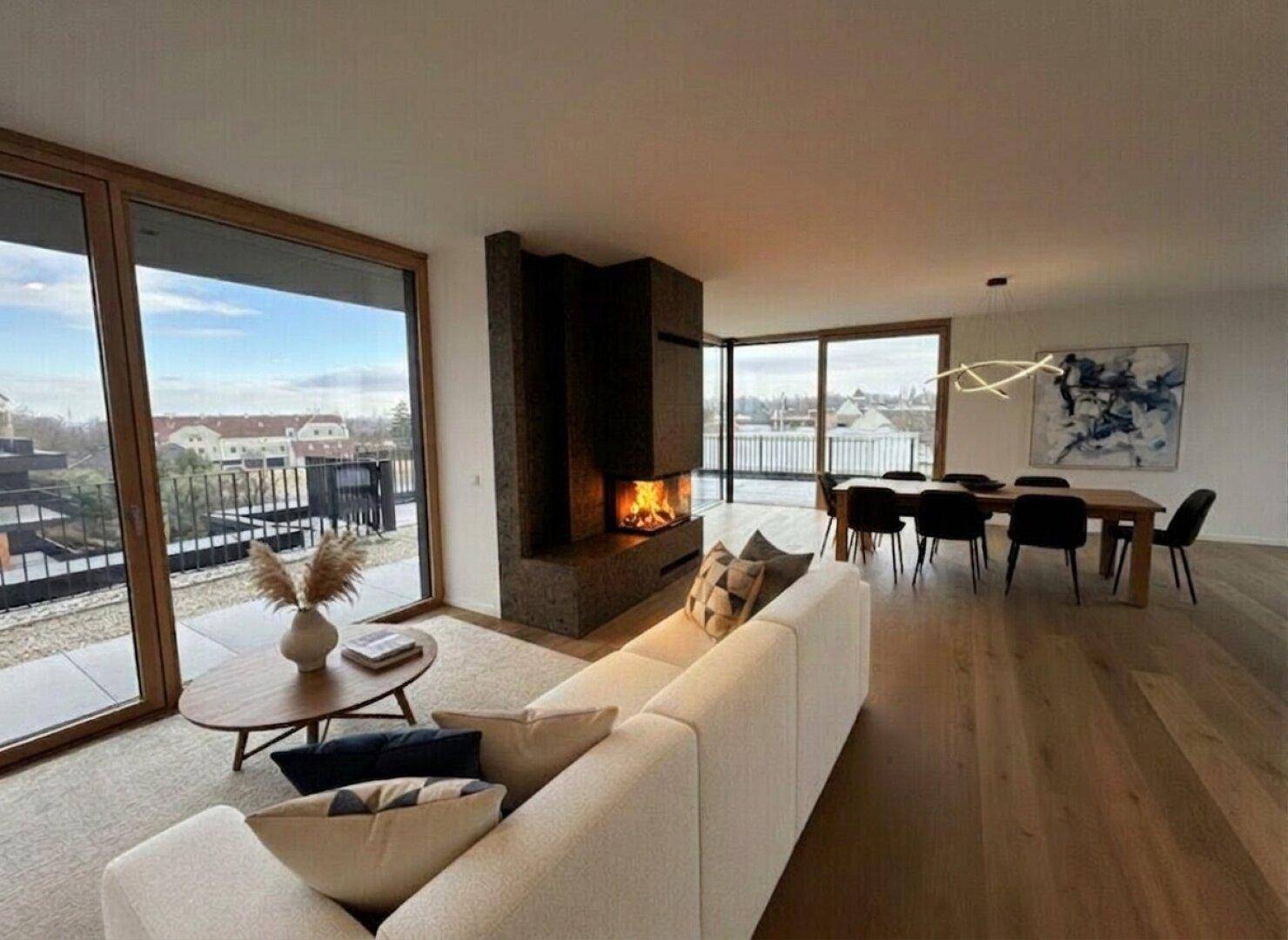 Heller Wohn-Essbereich mit modernem Kamin, Holzboden und großen Fenstern mit Ausblick.
