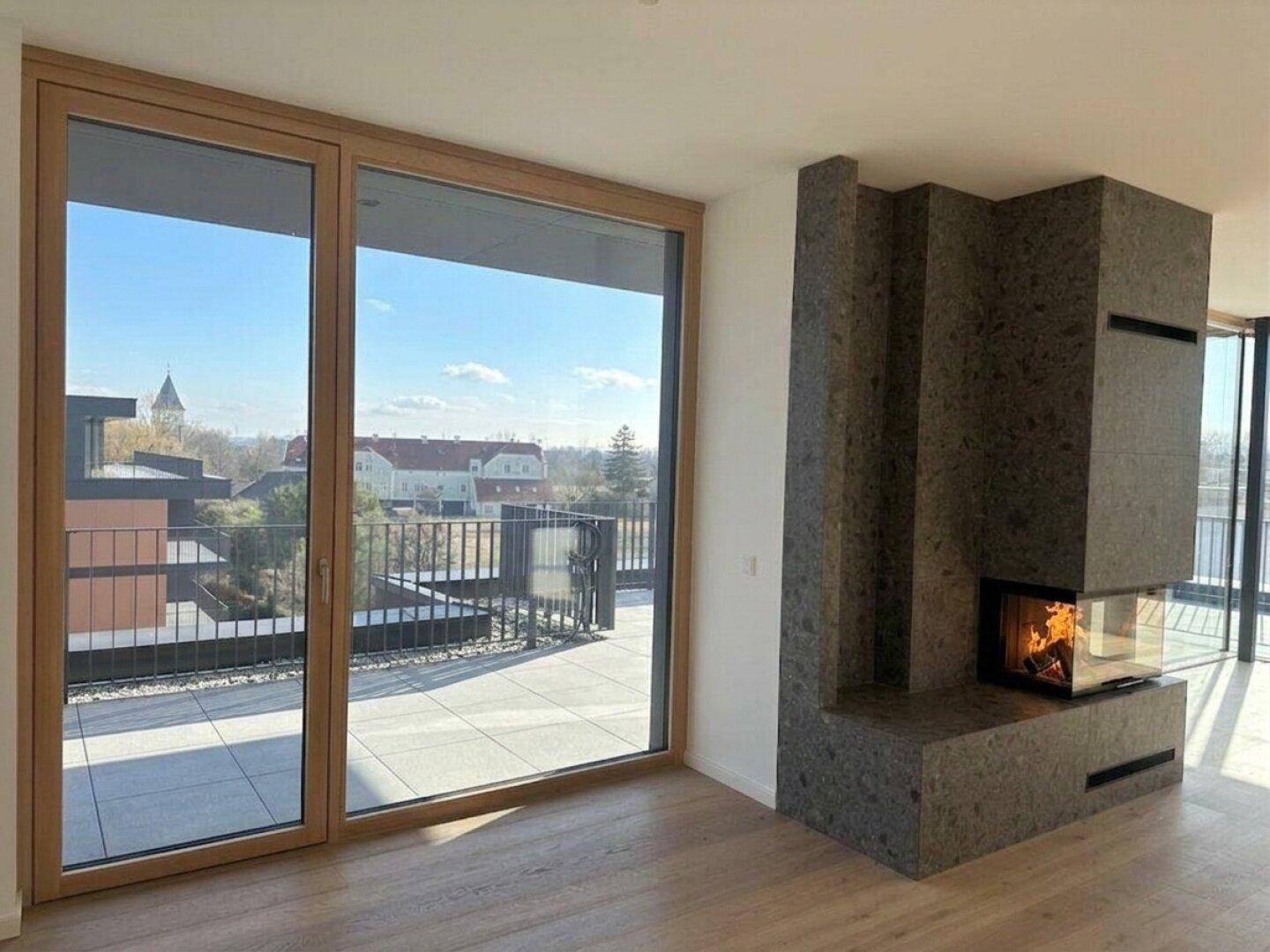 Wohnzimmer mit modernem Steinkamin und großen Schiebetüren zur sonnigen Terrasse.