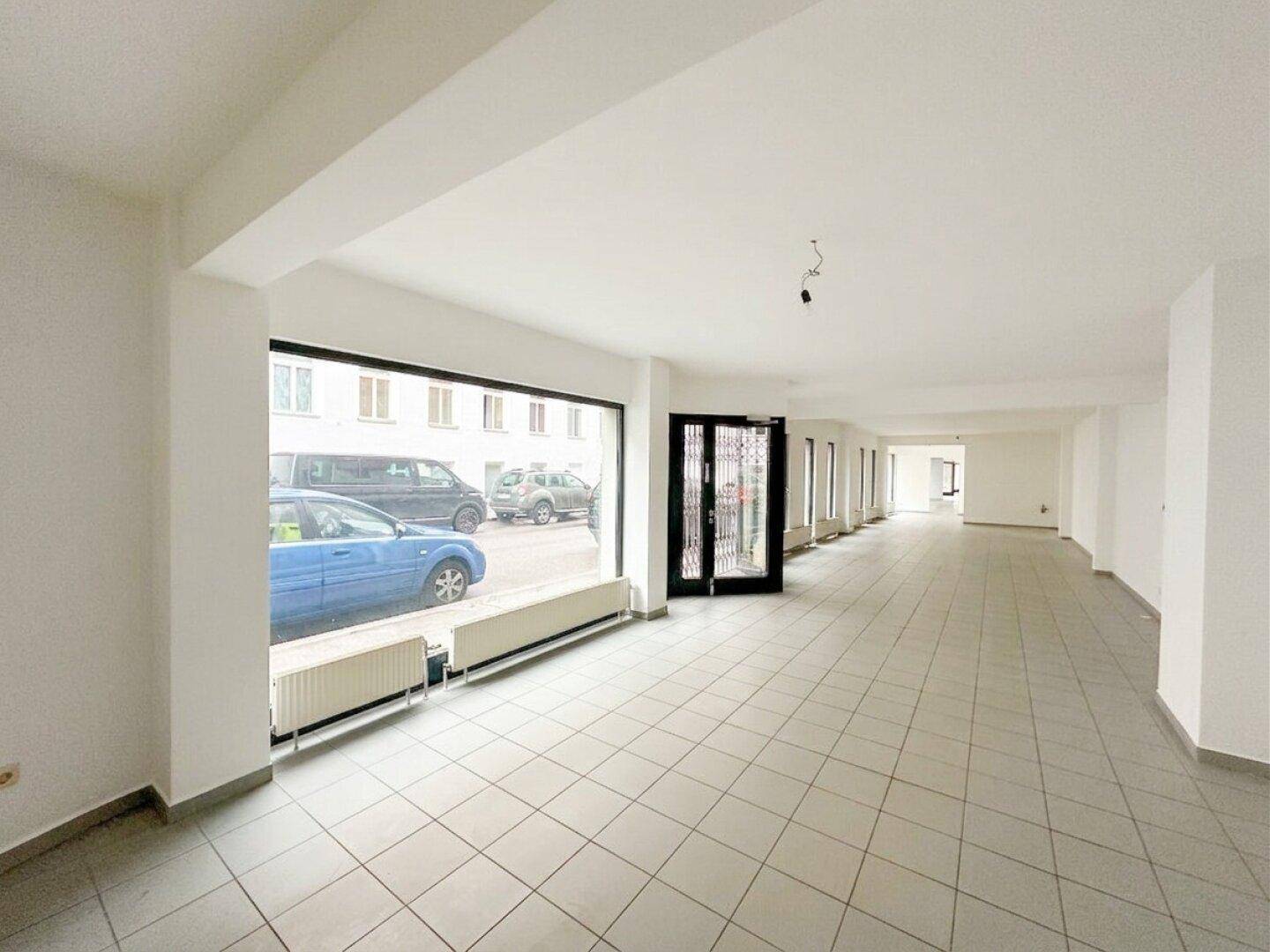 Weitläufiger Gewerberaum mit großer Fensterfront und hellem Fliesenboden, bereit zur individuellen Gestaltung.