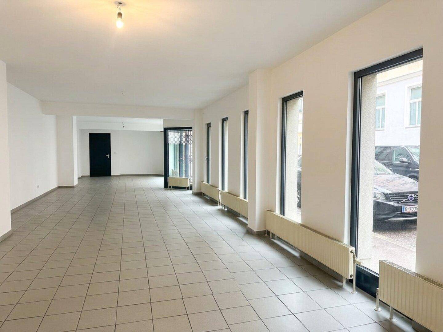 Langer, heller Gewerberaum mit durchgehenden Fliesen und vielen Fenstern, bietet vielseitige Nutzungsmöglichkeiten.