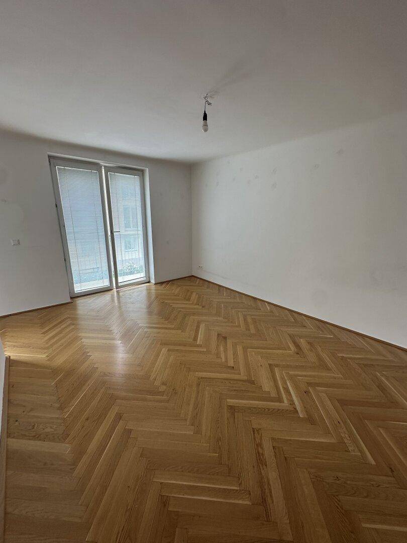 Helles Schlafzimmer mit Fischgrätparkett und großen Fenstern für viel Tageslicht.