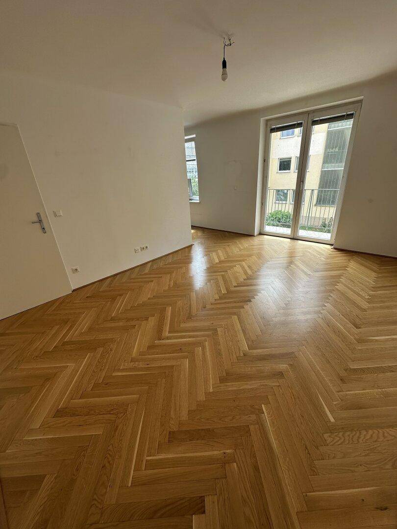 Geräumiges Wohnzimmer mit Fischgrätparkett und Zugang zu einem Balkon oder einer Terrasse.