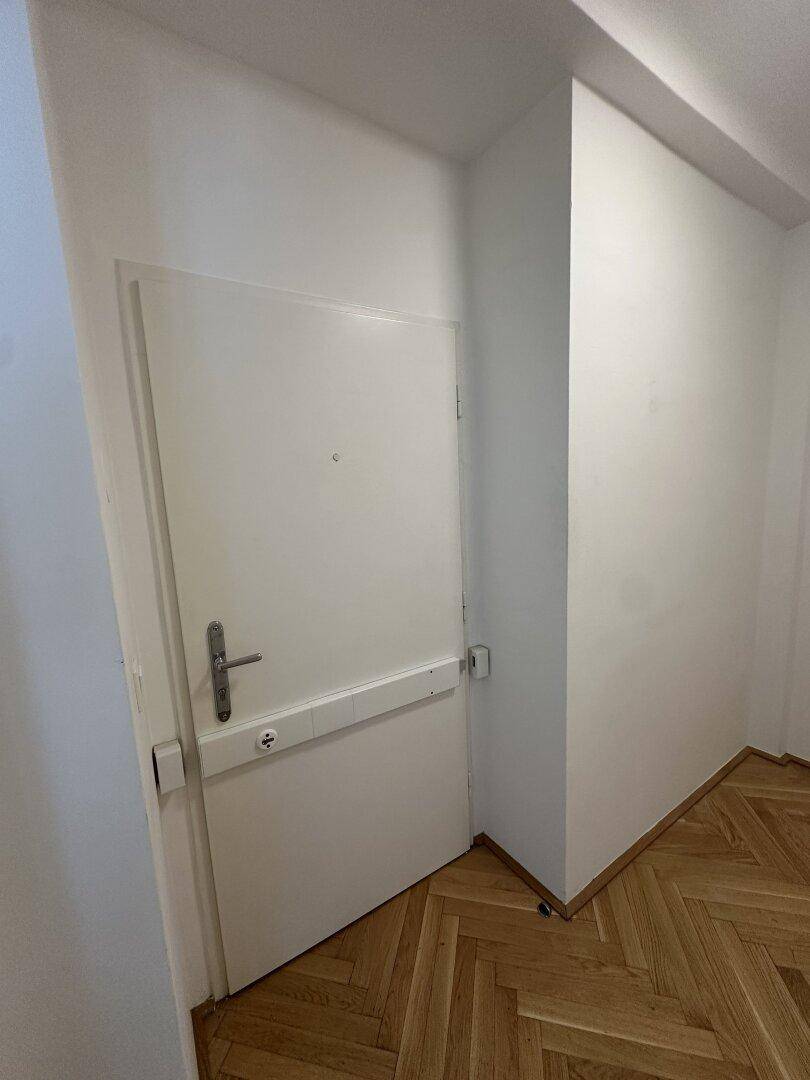 Schlichter Flur mit weißer Tür und Fischgrätparkett, der zu den Wohnräumen führt.