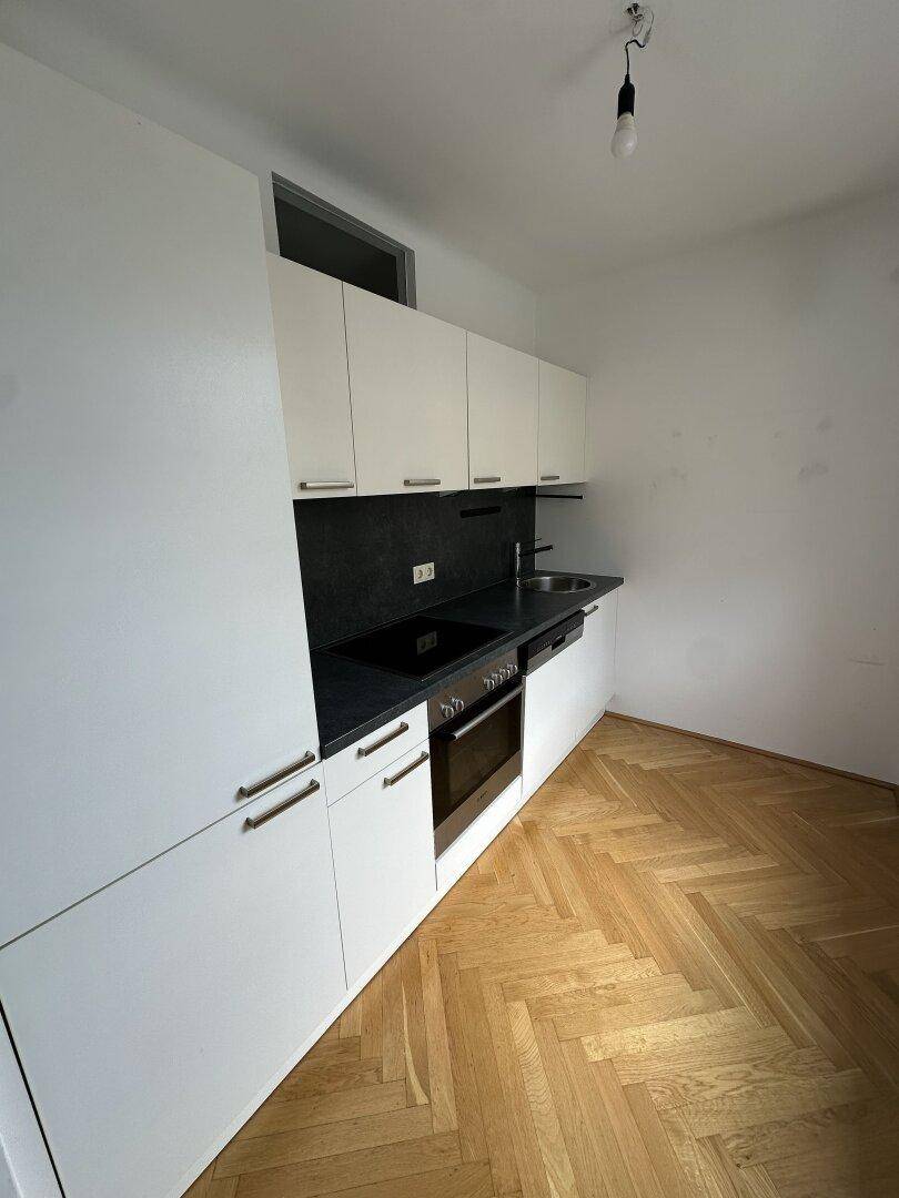 Moderne Einbauküche mit weißen Schränken, dunkler Arbeitsplatte und Fischgrätparkett.