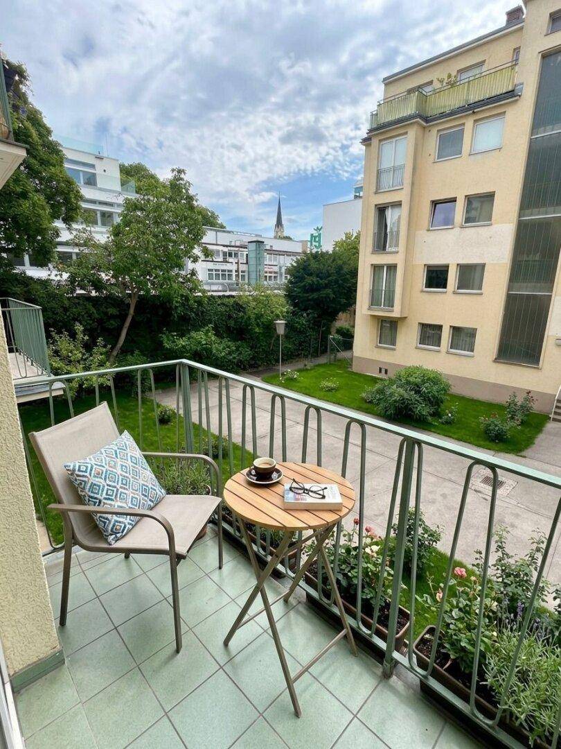 Gemütlicher Balkon mit Sitzgelegenheiten und Blick auf den begrünten Innenhof.