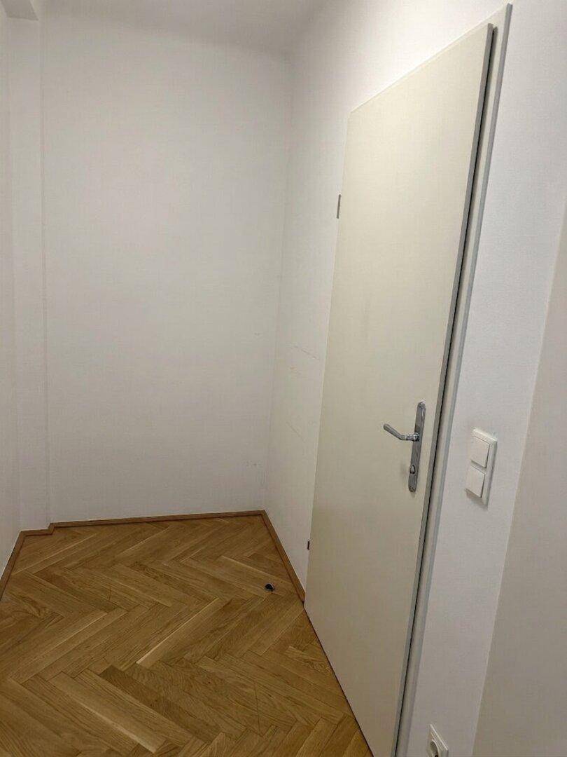 Heller Flur mit weißer Tür und Fischgrätparkett, der den Zugang zu den Räumen ermöglicht.