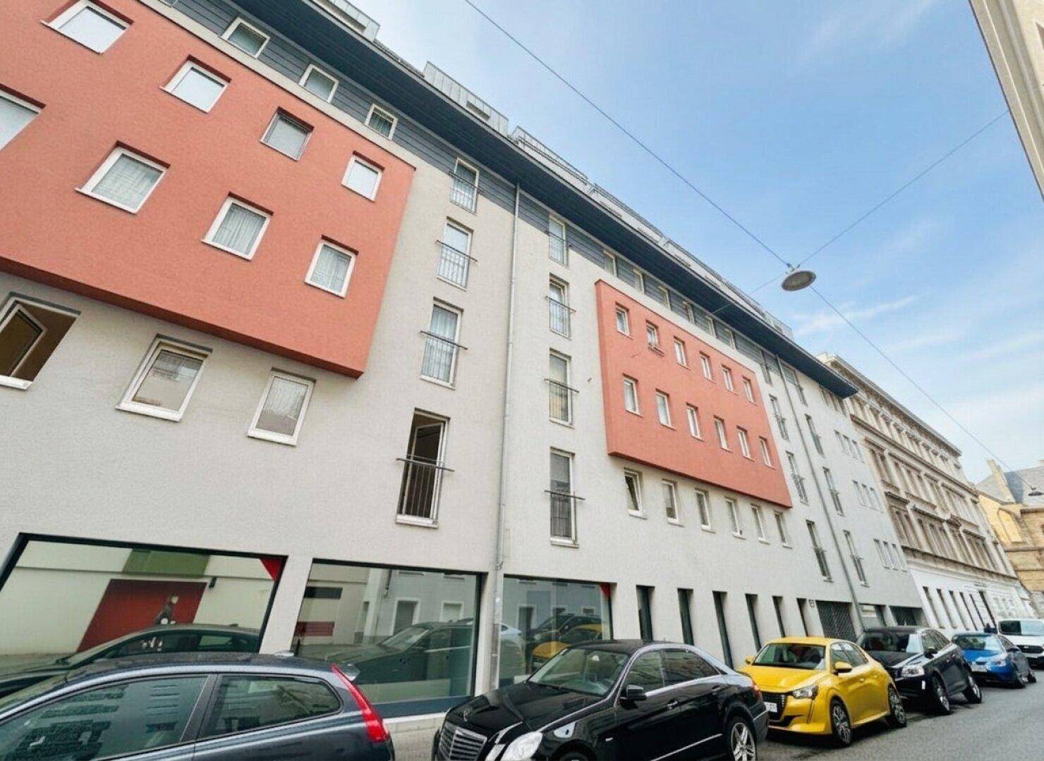 Ansicht der modernen Gebäudefassade mit grauen und orangefarbenen Abschnitten entlang einer belebten Straße.