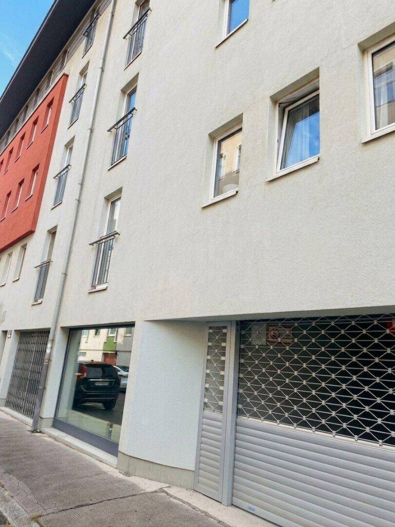 Detailansicht der Gebäudefassade im Erdgeschoss mit großem Fenster und geschlossenem Rollladen.