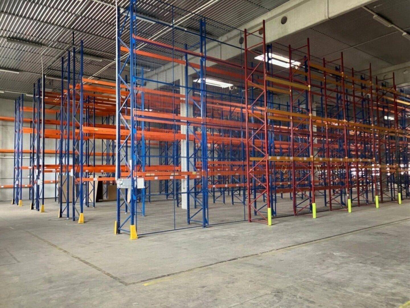Innenansicht einer Lagerhalle mit zahlreichen leeren Hochregalen und Betonboden.