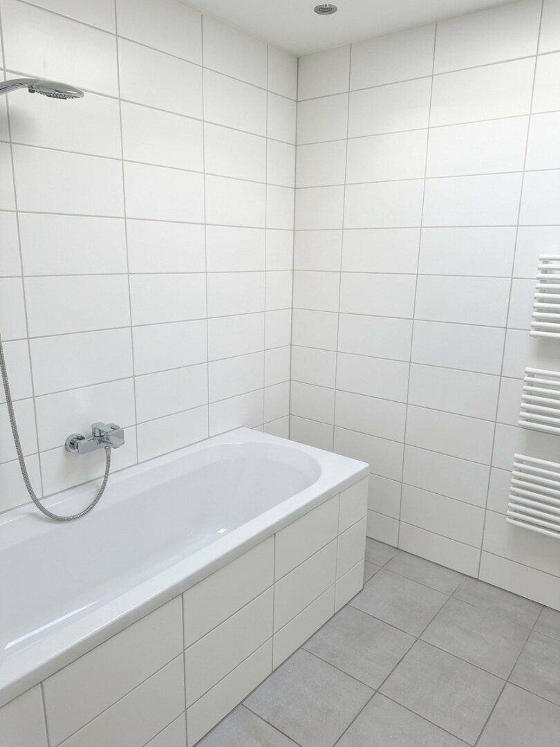 Helles Badezimmer mit Badewanne, Duschfunktion und beheiztem Handtuchtrockner.