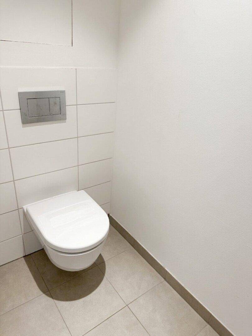 Separates WC mit wandhängender Toilette und modernen Fliesen an der Wand.