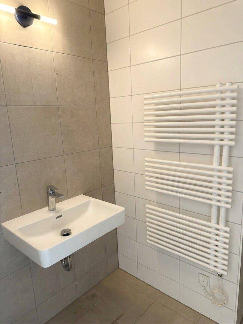 Modernes Badezimmer mit wandhängendem Waschbecken, Fliesen und beheiztem Handtuchhalter.