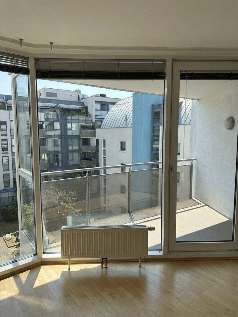 Heller Wohnraum mit großen Fenstern, Holzboden und Zugang zu einem Balkon mit Stadtblick.