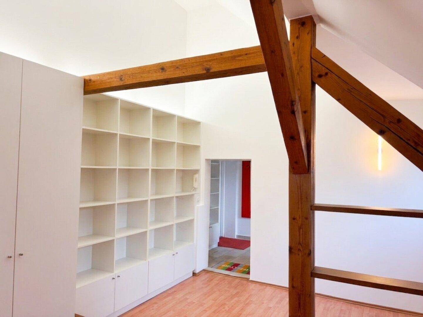 Dachbodenraum mit Holzbalken, Laminatboden und integrierten Regalen.