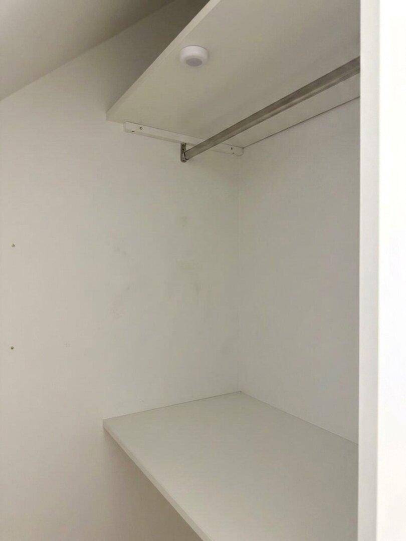 Einfacher Wandschrank mit Kleiderstange und Regalböden für Stauraum.